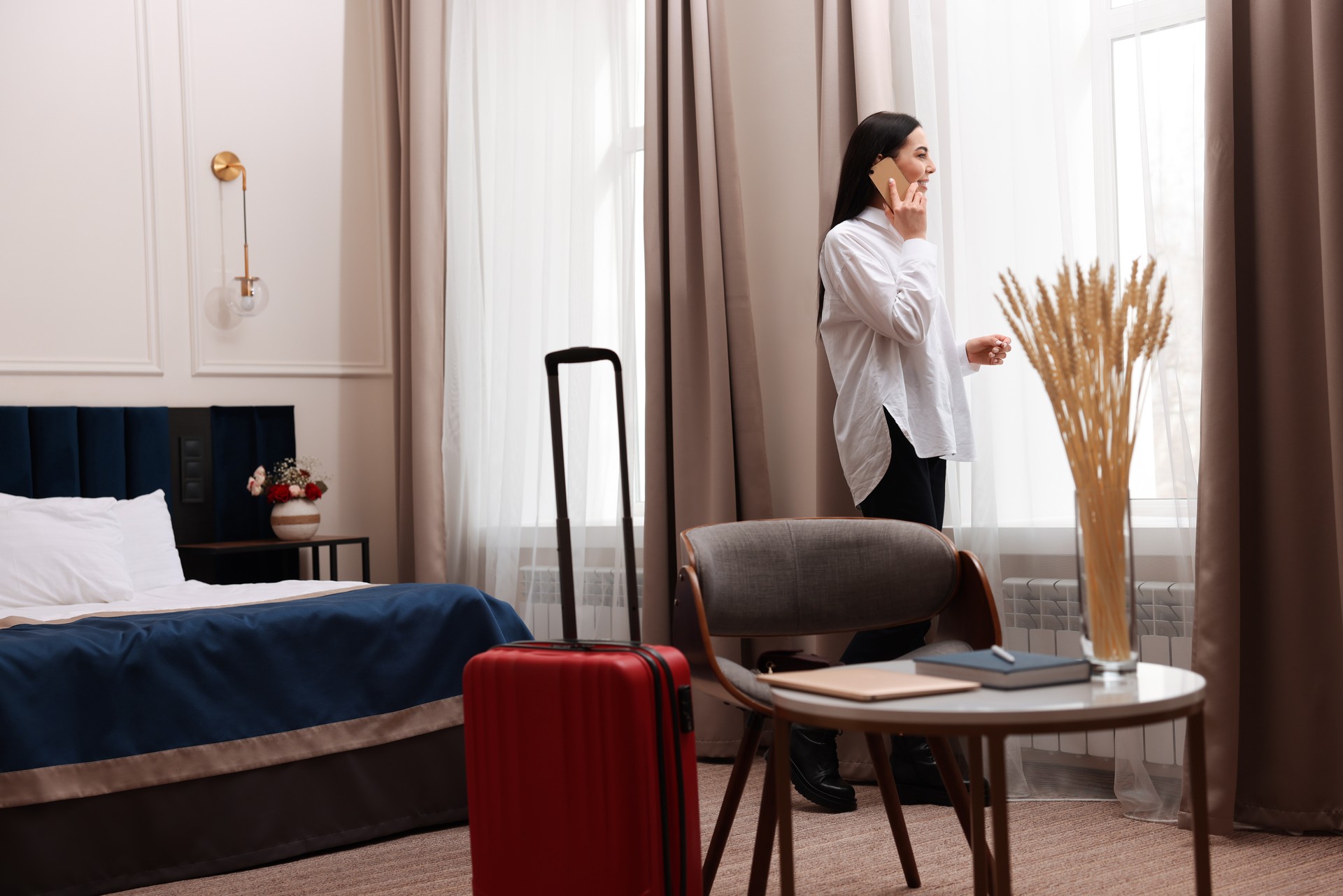 Beautiful businesswoman talking on phone near window in hotel room